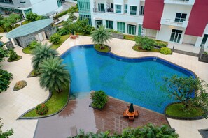 A swimming pool surrounded by palm trees and greenery, with a building in the background. - 2 Bedrooms Woodland Park Apartment by Travelio (Jakarta)