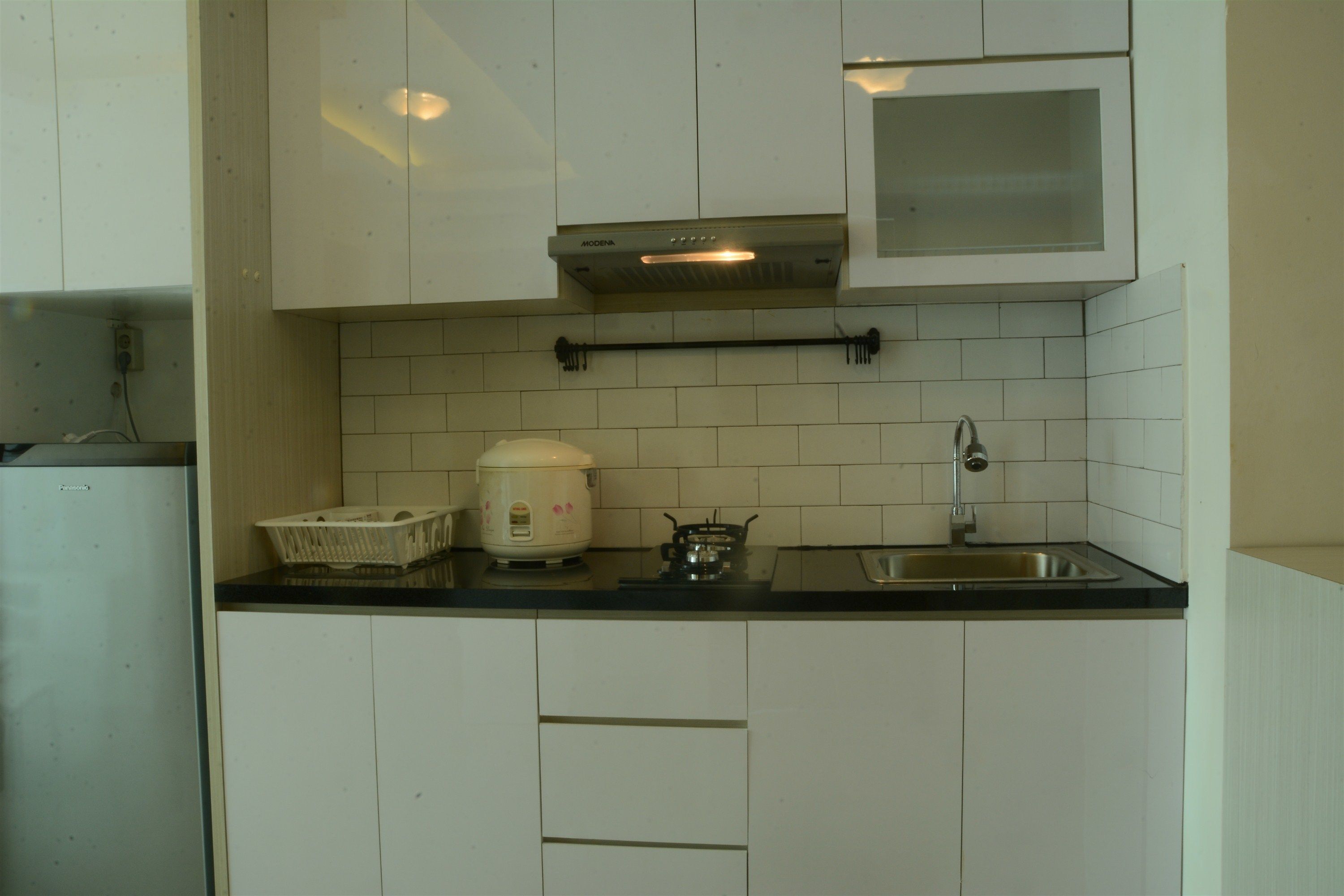 A kitchen with white cabinets, a stove, a sink, and a rice cooker.