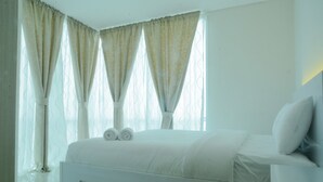 A bedroom with a bed, curtains, and a nightstand. - 2 Bedrooms Woodland Park Apartment by Travelio (Jakarta)