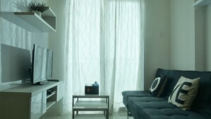A modern living room with a flat-screen TV, a sofa with decorative pillows, a small table, and a potted plant on a shelf. - 2 Bedrooms Woodland Park Apartment by Travelio (Jakarta)