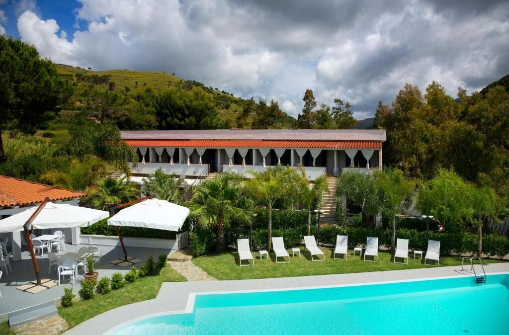 A resort with a swimming pool, lounge chairs, and a building with a red-tiled roof.