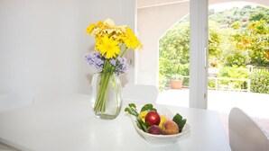 Una mesa blanca con un jarrón de flores amarillas y un frutero.