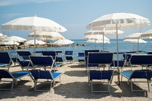 A beach with rows of blue lounge chairs and white umbrellas, facing a calm sea. - Baia Marticana Residence Hotel  (Montecorice)