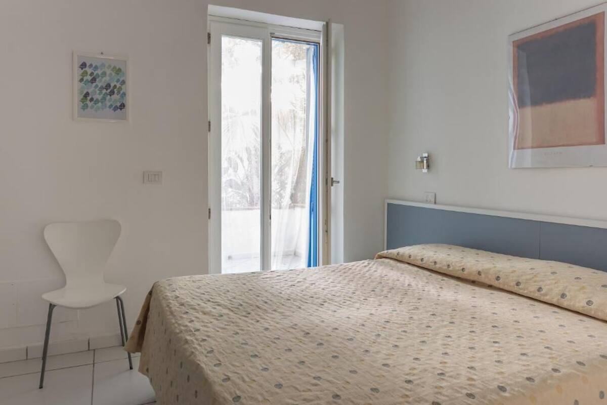 Een slaapkamer met een bed, een stoel en een deur naar een balkon.