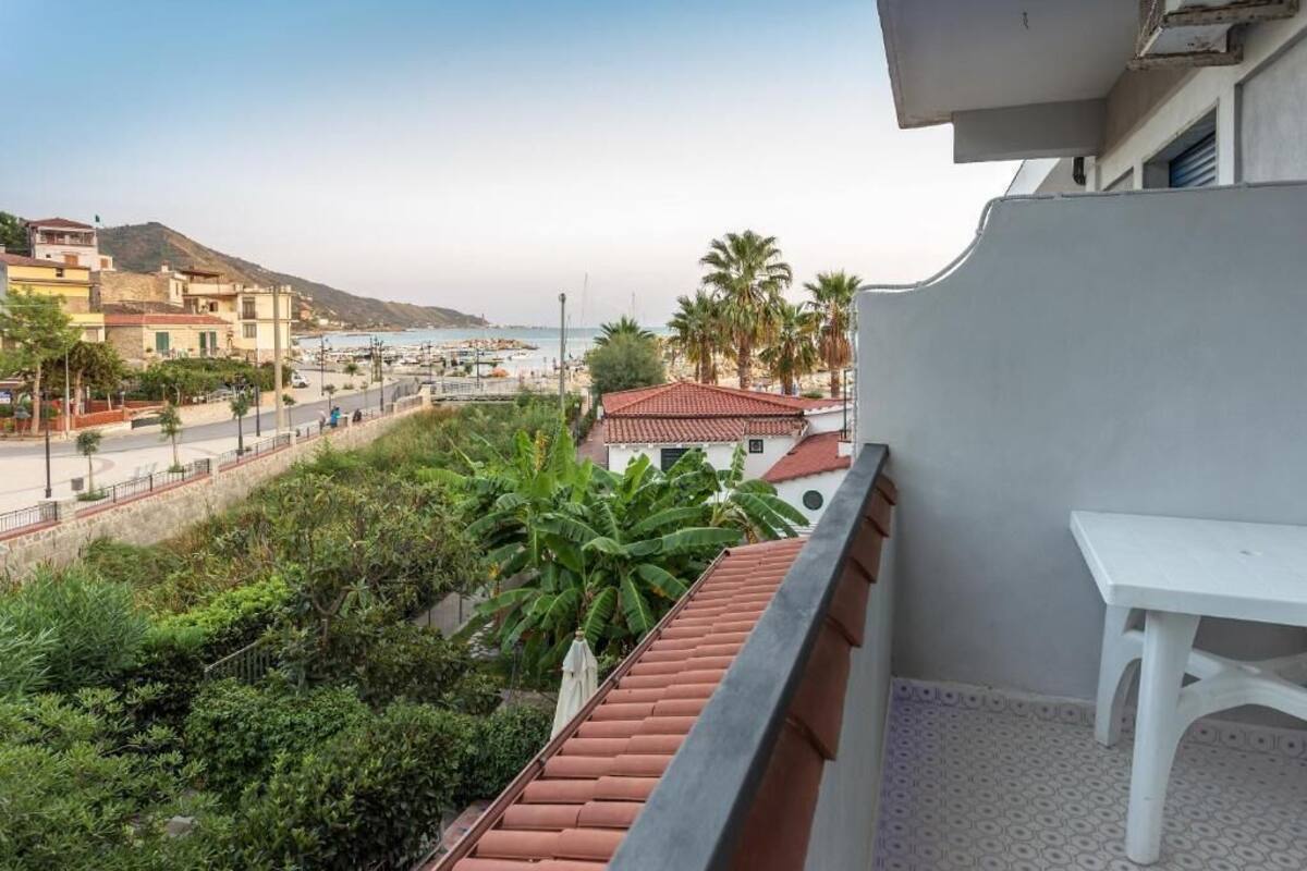 Een balkon met uitzicht op een strand, palmbomen en een weg.