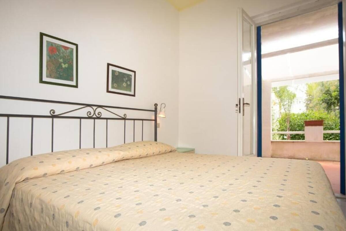 Een slaapkamer met een bed, twee ingelijste foto's aan de muur en een raam met uitzicht op groen.
