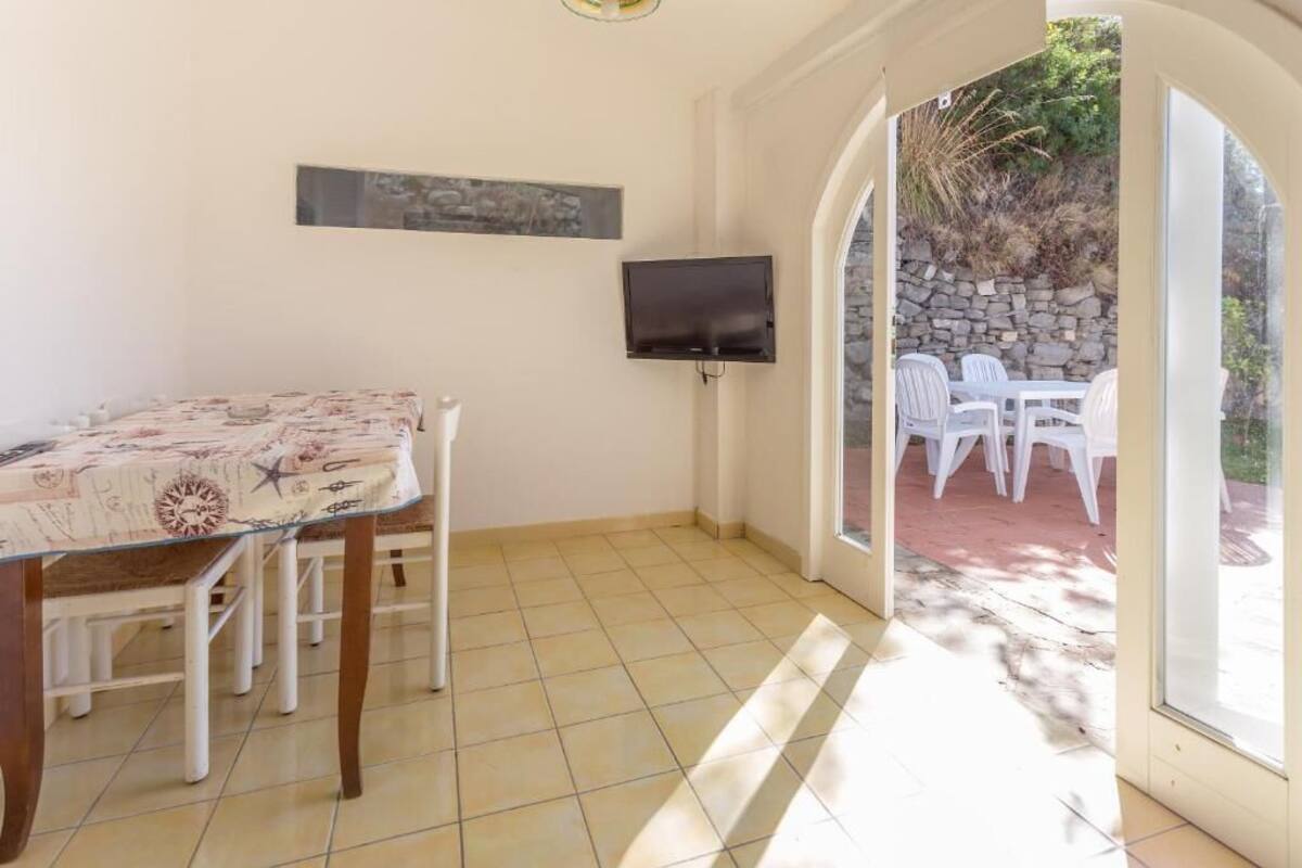 Een eetruimte met een tafel en stoelen, een flatscreen televisie aan de muur en uitzicht op een terras met stoelen.