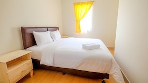 A neatly made bed with white linens, a wooden nightstand, and a yellow curtain on a window. - 2 Bedrooms at Grand Palace Kemayoran Apartment by Travelio (Jakarta)