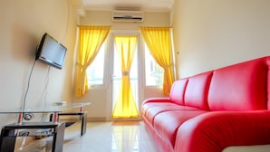 A living room with a red sofa, a glass coffee table, a flat-screen TV, and yellow curtains. - 2 Bedrooms at Grand Palace Kemayoran Apartment by Travelio (Jakarta)