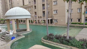 A swimming pool with a gazebo, palm trees, and a multi-story building in the background. - 2 Bedrooms at Grand Palace Kemayoran Apartment by Travelio (Jakarta)