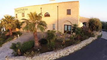 A building with the name "RuriPulcra" on the facade, surrounded by palm trees and a gravel pathway.