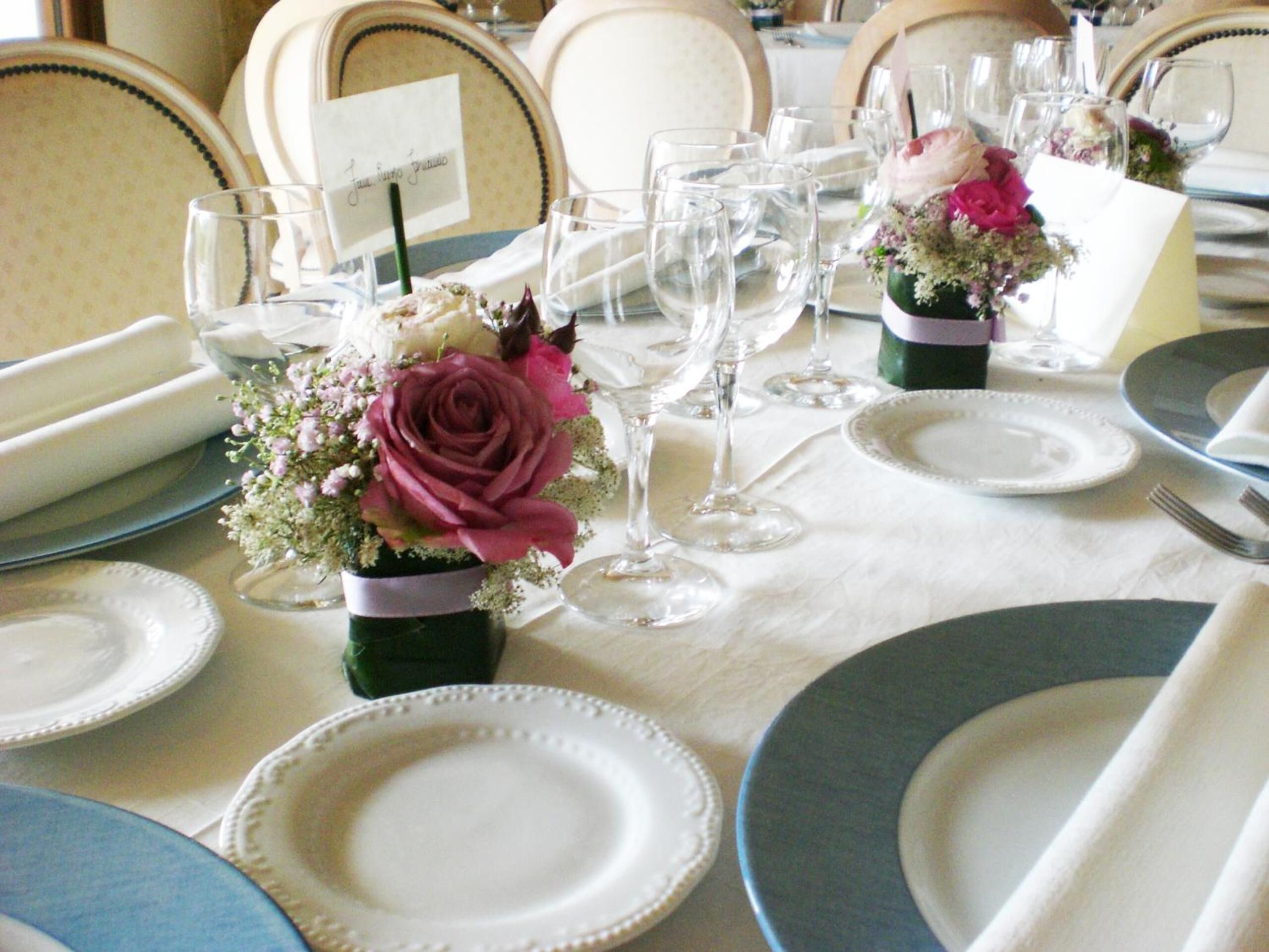 A table set for a formal event with white and blue plates, clear glasses, and small vases with flowers.