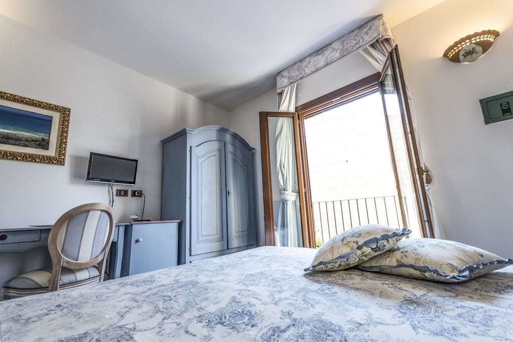 A bedroom with a bed, a desk, a chair, a wardrobe, a television, and a window with curtains.