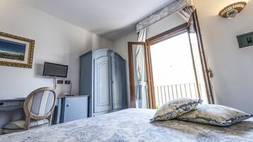 A bedroom with a bed, a desk, a chair, a wardrobe, a television, and a window with curtains.