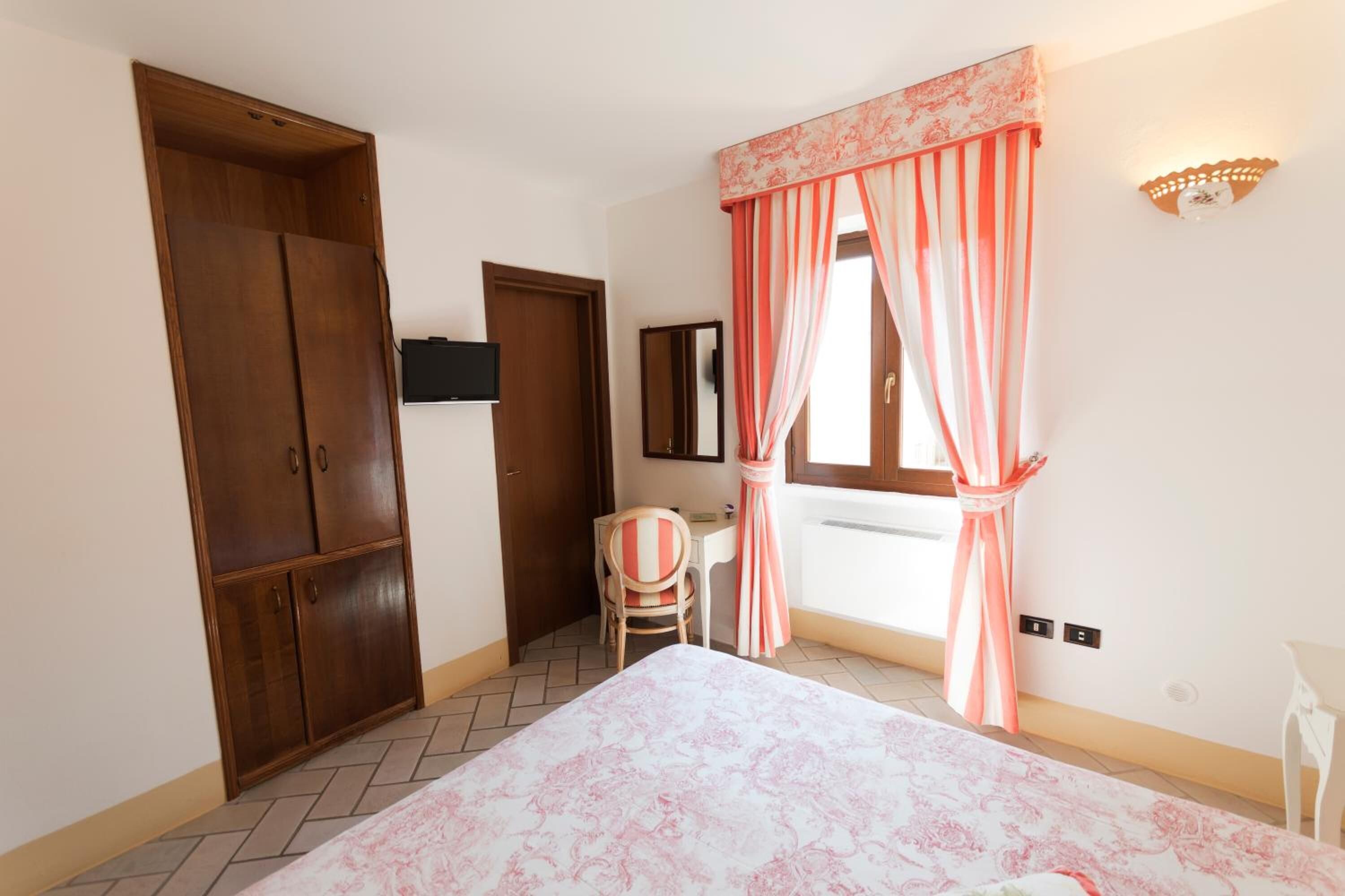 A bedroom with a bed, wardrobe, desk, chair, and window with curtains.