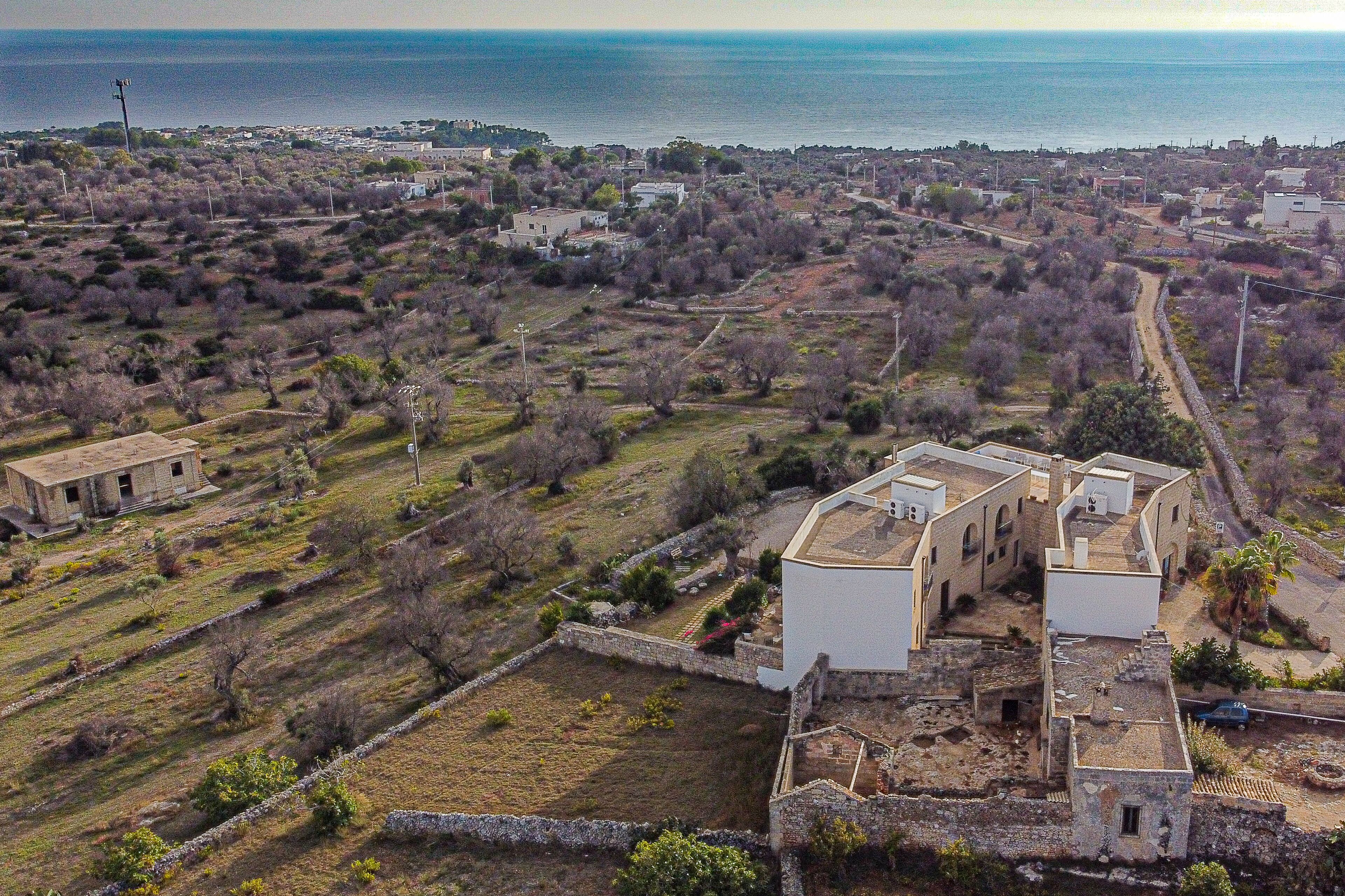 Vista aérea de un pueblo costero con un complejo de edificios blancos destacado, rodeado de campos abiertos y vegetación escasa.