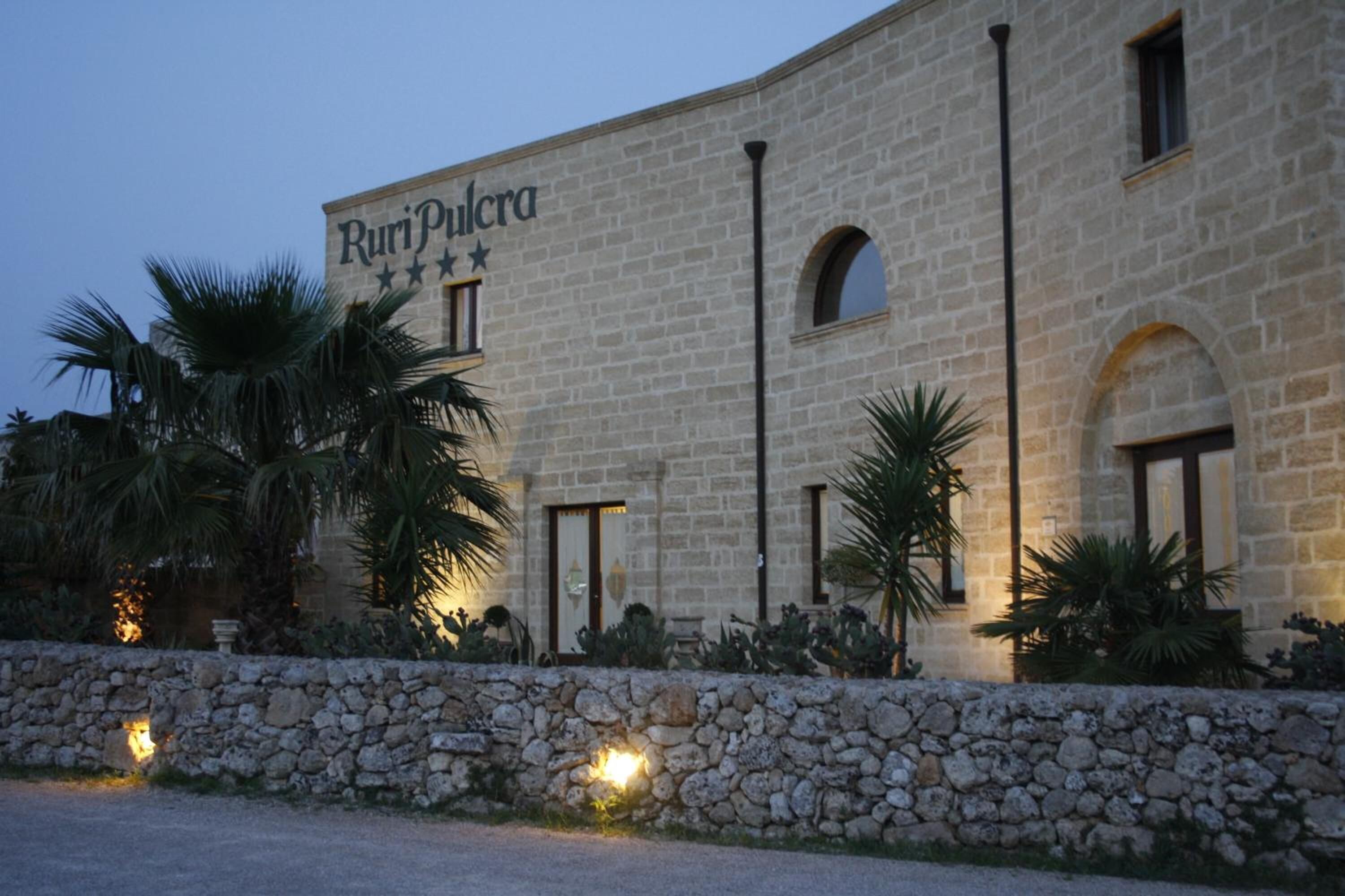 A stone building with the name "Ruripulcra" on the facade, featuring arched windows and a stone wall with lights.