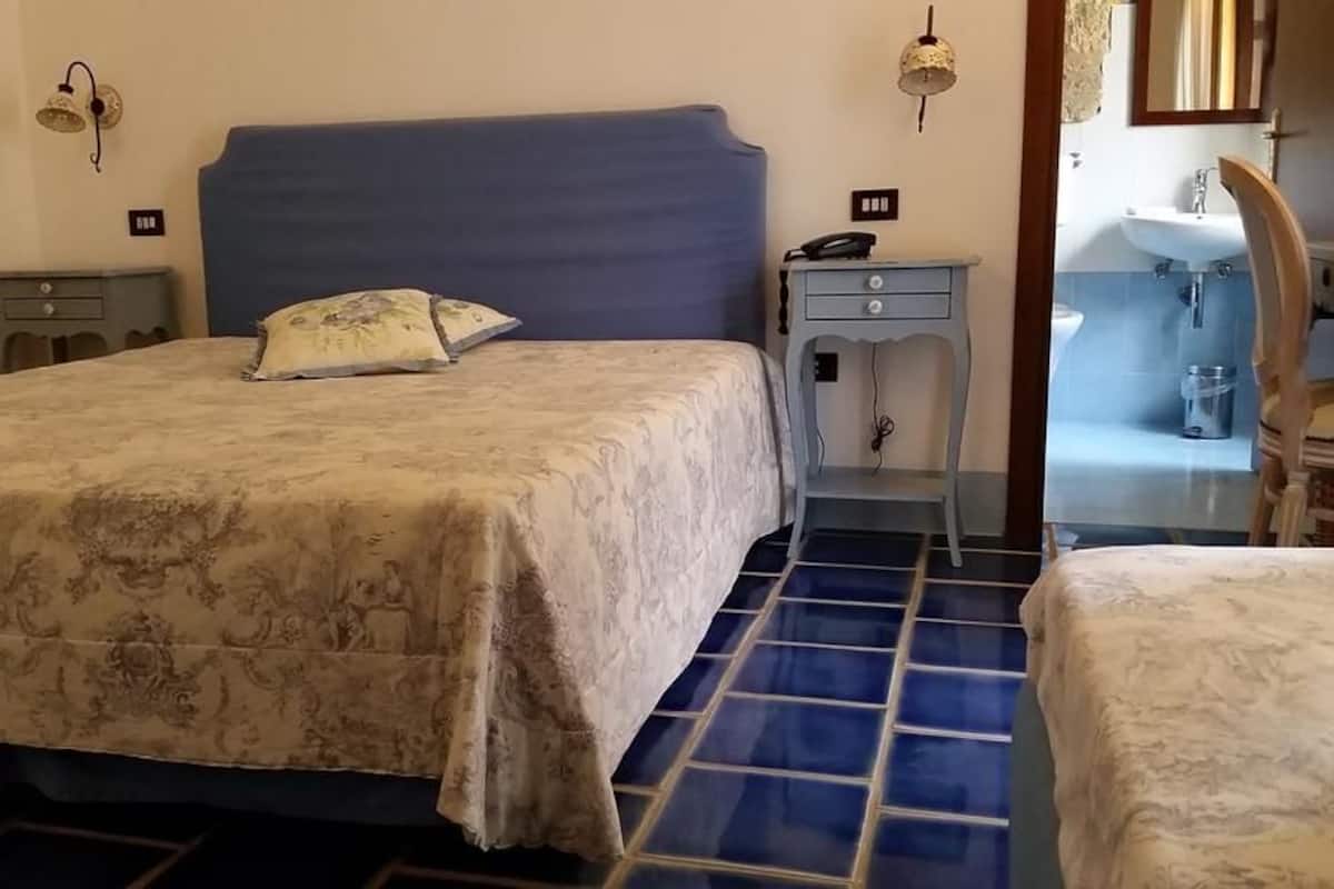 Una camera da letto con un letto, comodini e un bagno parzialmente visibile attraverso una porta aperta.