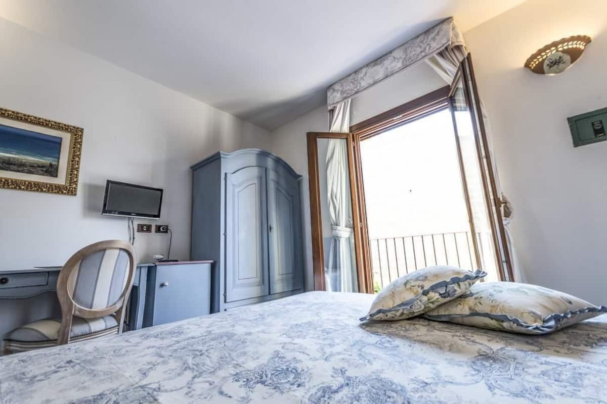 Una camera da letto con un letto, una scrivania, una sedia, un armadio, una televisione e una finestra con tende.
