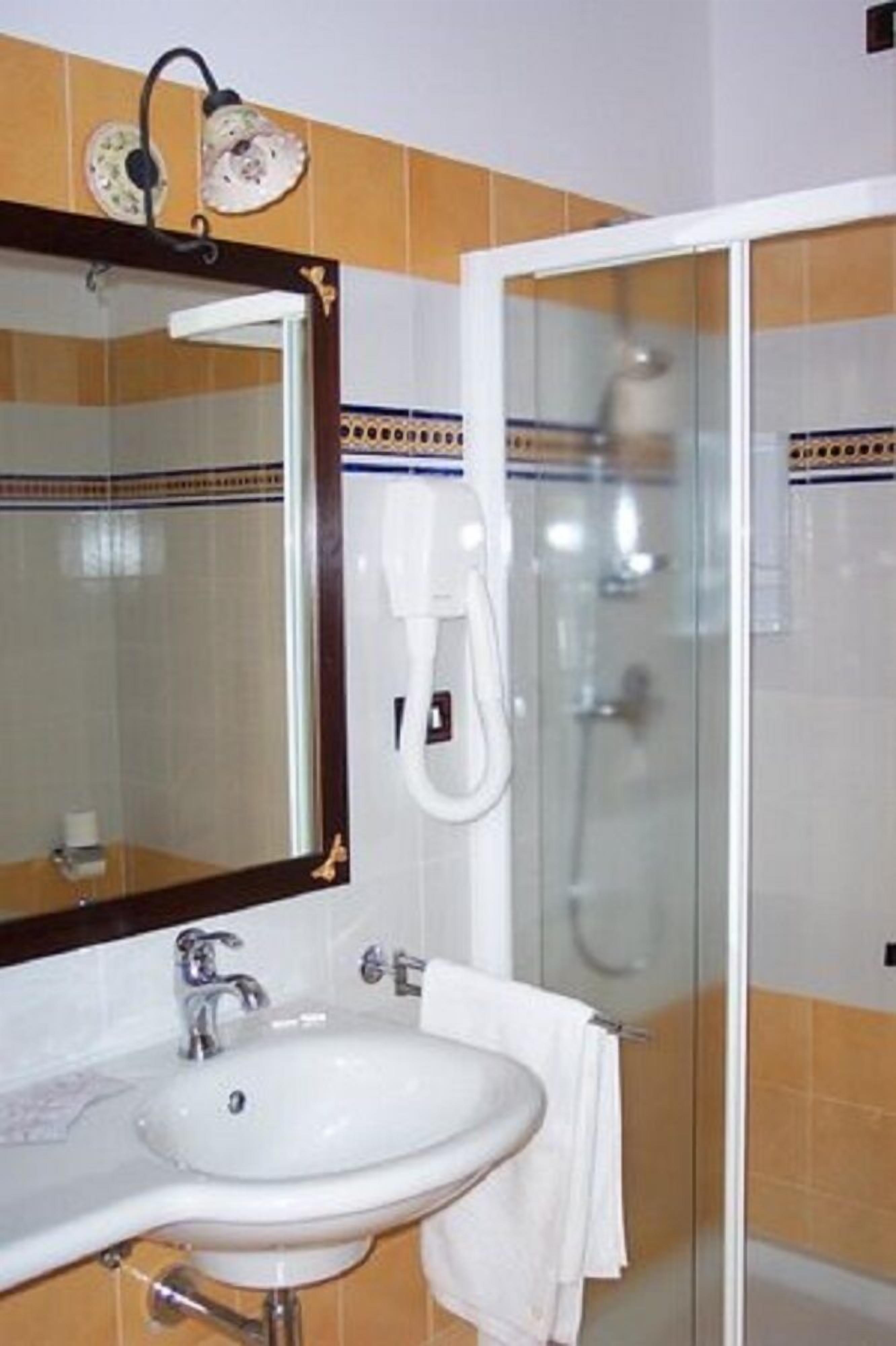 Un baño con lavamanos blanco, un espejo con marco decorativo y una cabina de ducha de vidrio.