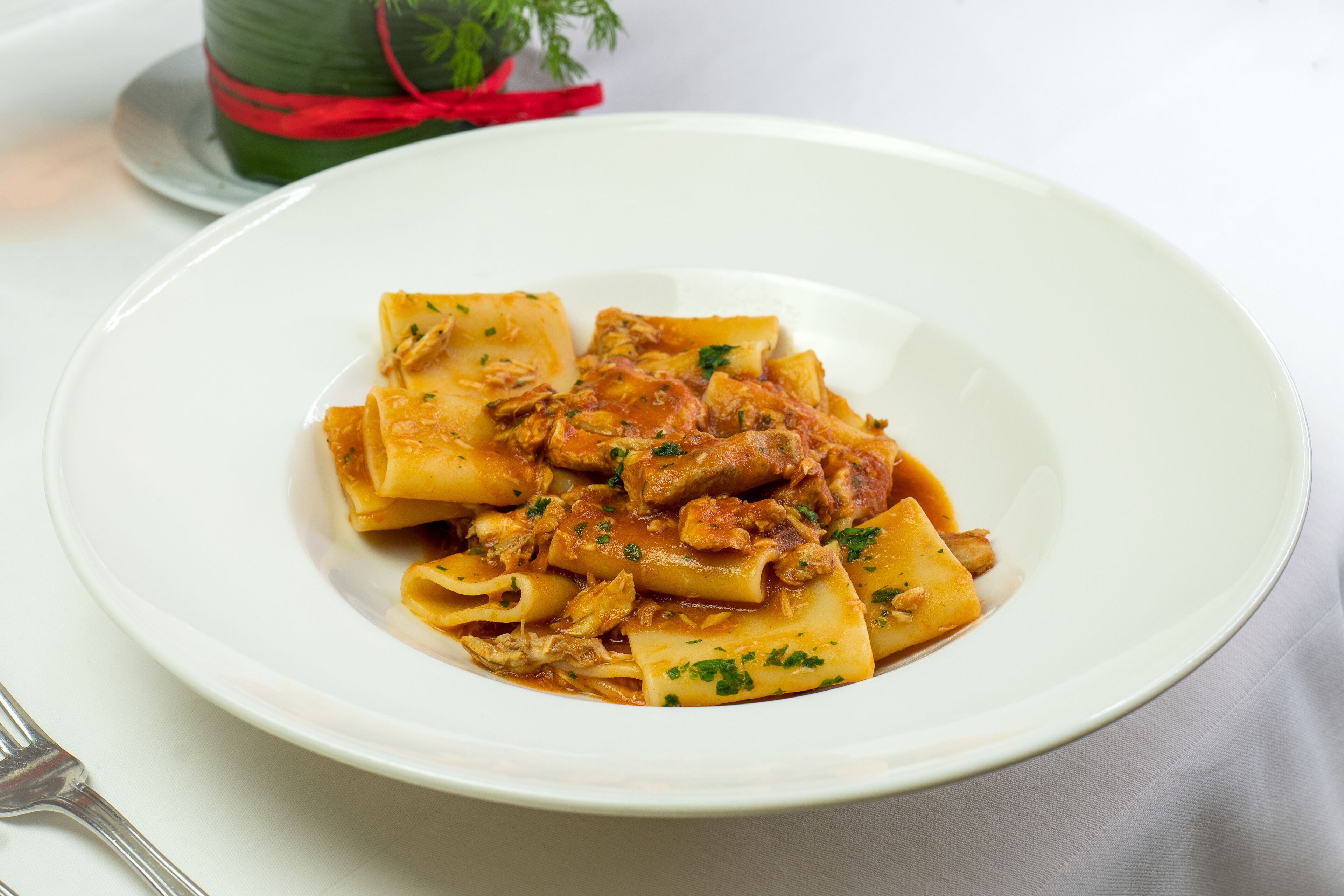 Prato de massa com molho de tomate e carne, decorado com ervas, sobre um prato branco.