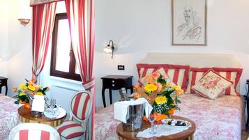 A hotel room with a bed, a dining table with chairs, a vase of flowers, and a painting on the wall.