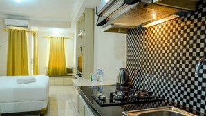 A compact hotel room with a kitchenette, a bed with a rolled-up towel, and a checkered backsplash. - Simply Studio Room at Grand Serpong Apartment By Travelio (Tangerang)