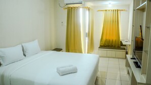 A hotel room with a bed, a TV, and curtains. - Simply Studio Room at Grand Serpong Apartment By Travelio (Tangerang)