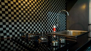 A kitchen with a black and white checkered backsplash, stainless steel sink, and modern appliances. - Simply Studio Room at Grand Serpong Apartment By Travelio (Tangerang)
