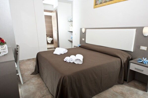 A neatly made bed with brown bedding, a bedside table with a lamp, and a small decorative item on the nightstand. - Hotel Aquarius (Cattolica)