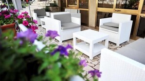 An outdoor seating area with white wicker furniture and a stone floor. - Hotel Aquarius (Cattolica)