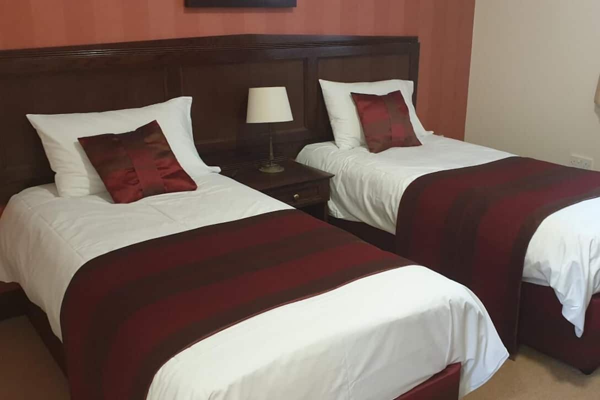 A hotel room with two single beds, each with a red and white striped blanket, white pillows, and a wooden headboard.