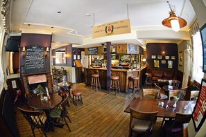 A cozy bar with wooden floors and stools, a counter with a menu, and a sign indicating the location in Hampshire. - The Flying Bull Inn (Liss)