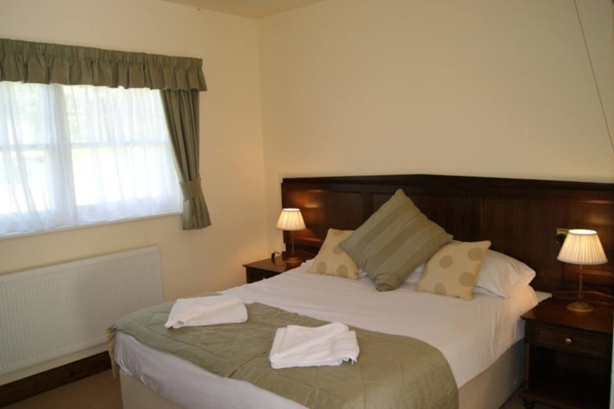 A neatly made bed with a green blanket, two bedside lamps, and a window with curtains.