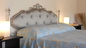 A bedroom with a tufted headboard, a bed with a blue patterned bedspread, a bedside table with a lamp, and a nightstand with a book and a decorative item. - B&B Bosco dei Cervi (Grizzana Morandi)