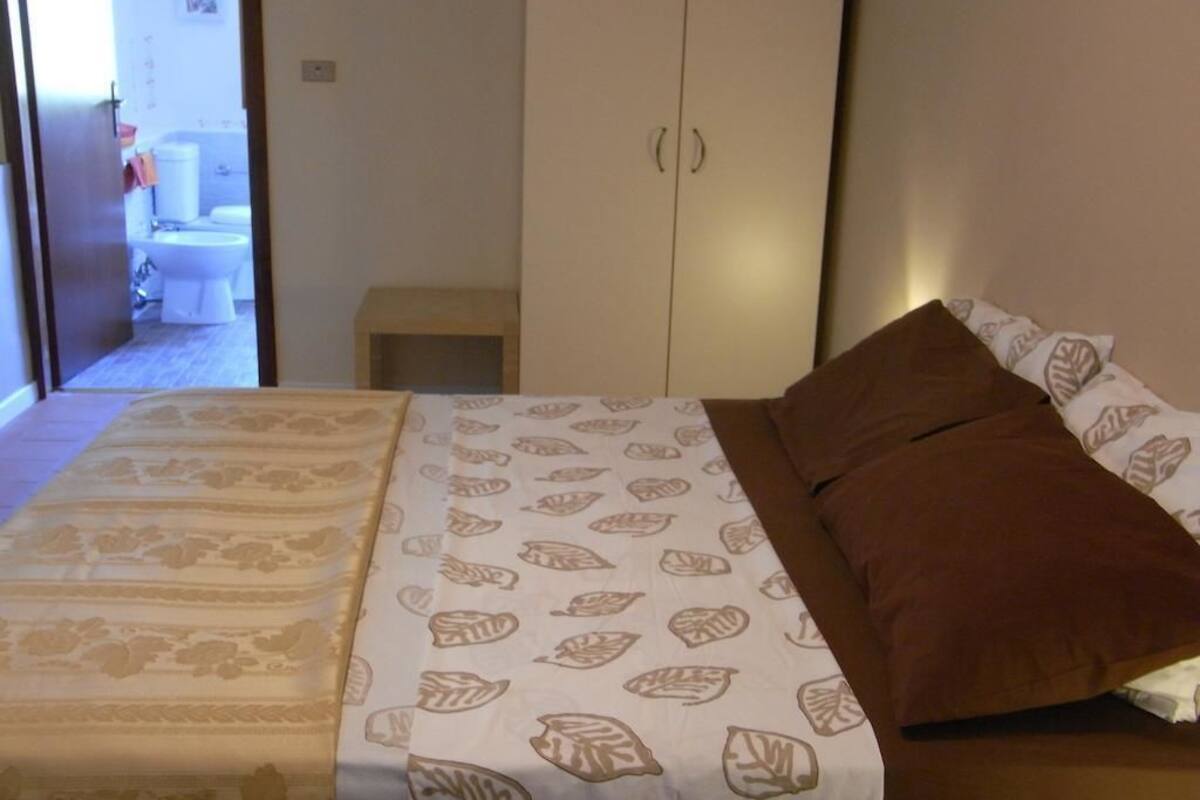 Ein Schlafzimmer mit Bett, Schrank und einem durchgegangenen Tür sichtbaren Badezimmer.