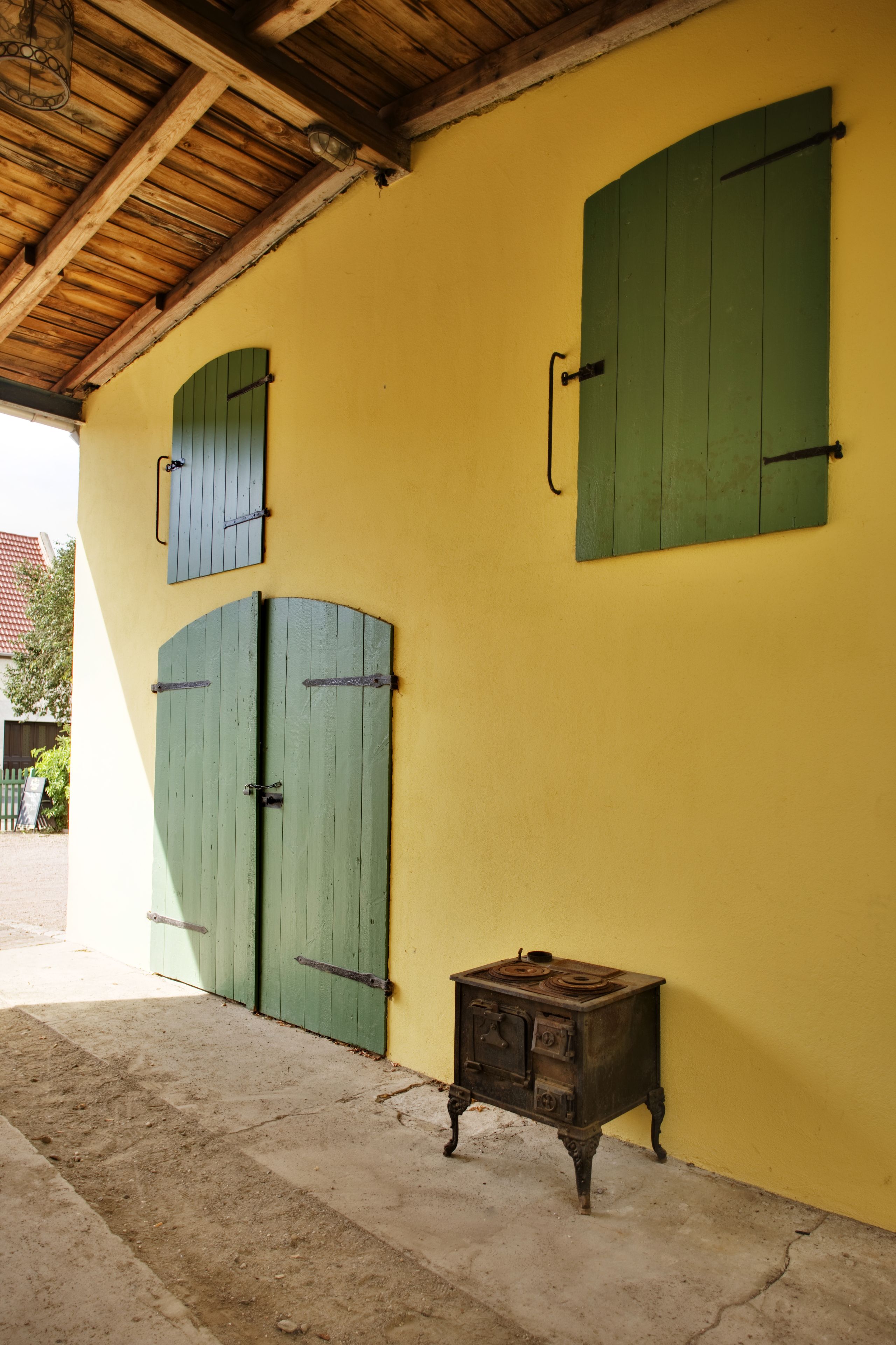 Pared amarilla con tres puertas verdes y una pequeña estufa de madera.