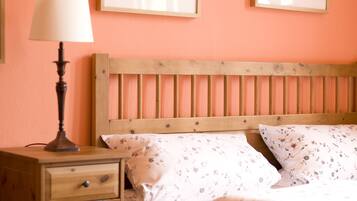 A bedroom with a wooden bed, a nightstand with a lamp, and two framed botanical prints on the wall.