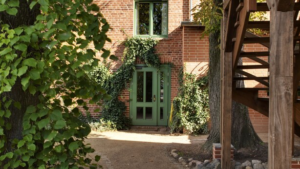 Een bakstenen gebouw met groene ramen en een houten constructie aan de rechterkant.