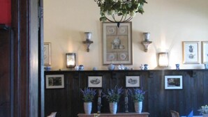 Een eetruimte met houten lambrisering, tafels met blauwe tafelkleden en potplanten.