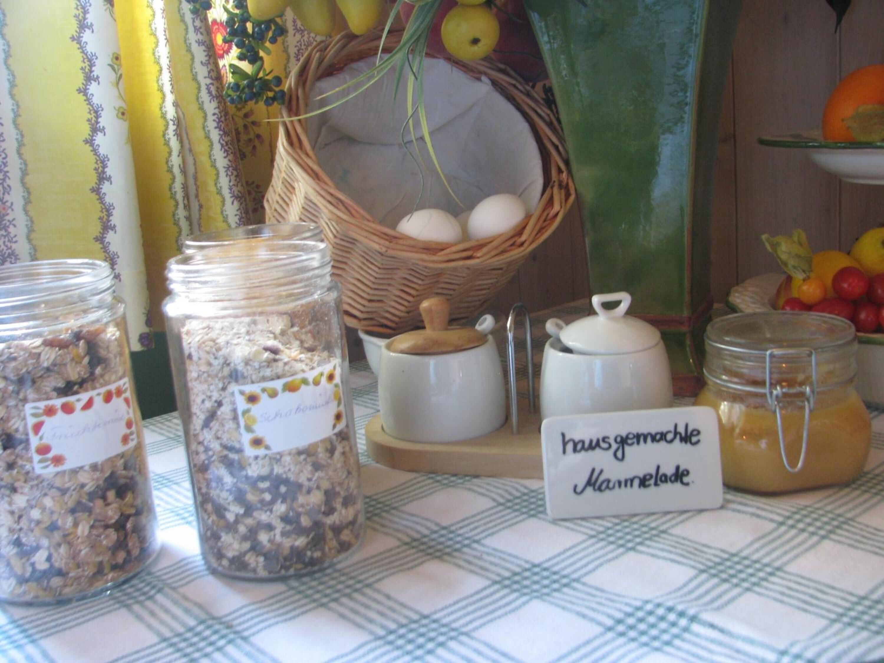 A table with jars of food, a basket of eggs, and a sign indicating 'Hausgemachte Marmelade'.