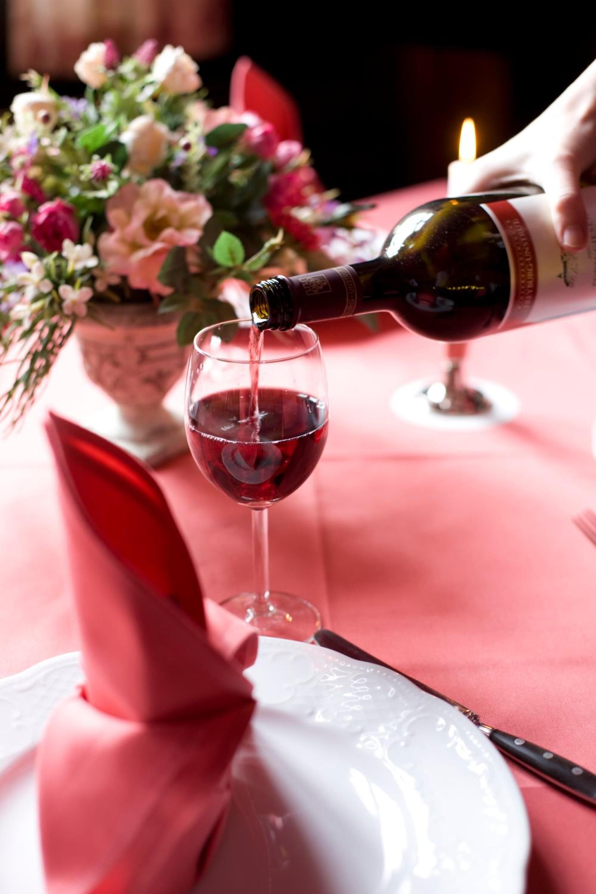 A bottle of red wine being poured into a glass.