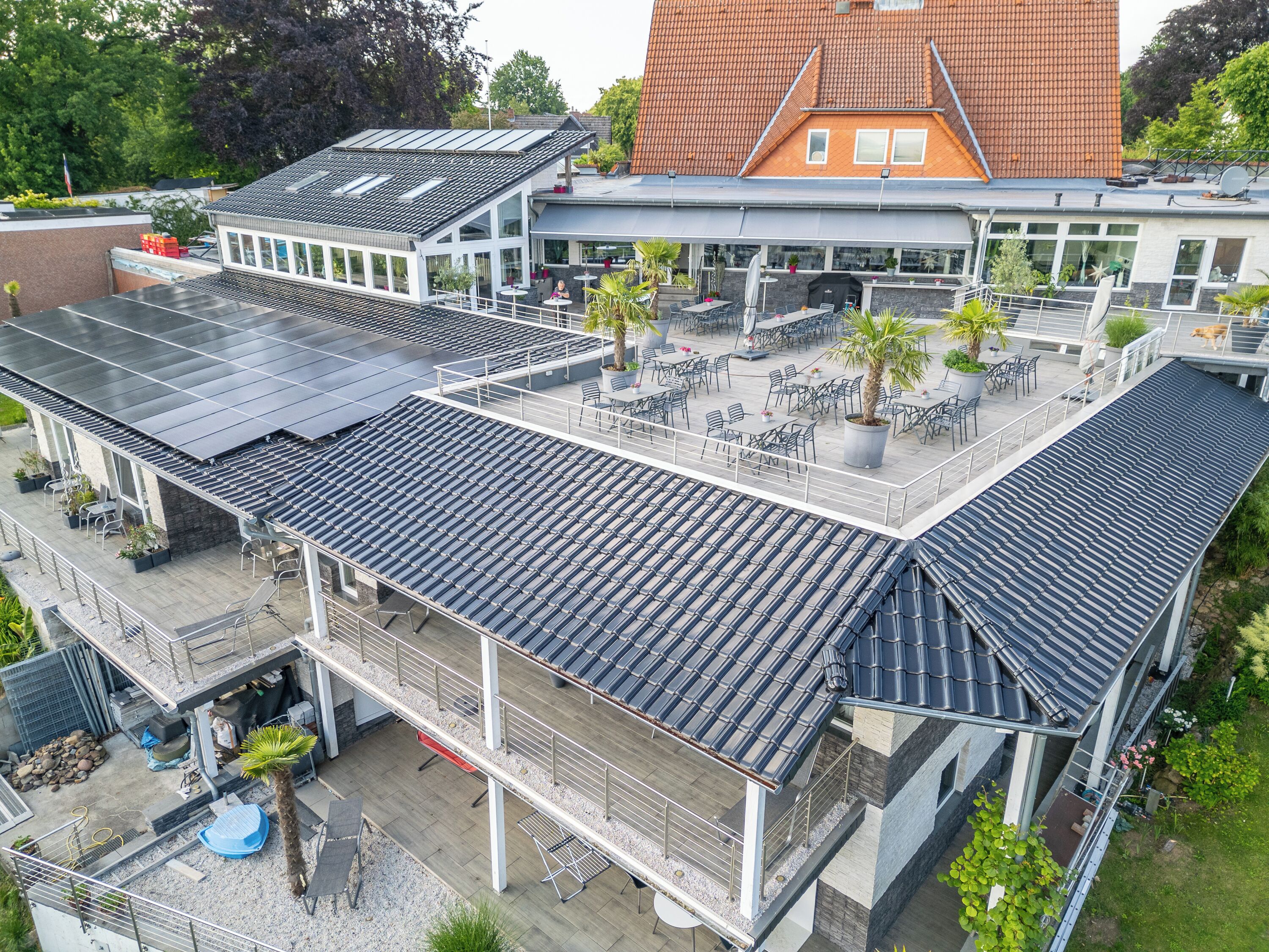 A rooftop terrace with multiple seating areas, a pool, and a view of a traditional building with a tiled roof.