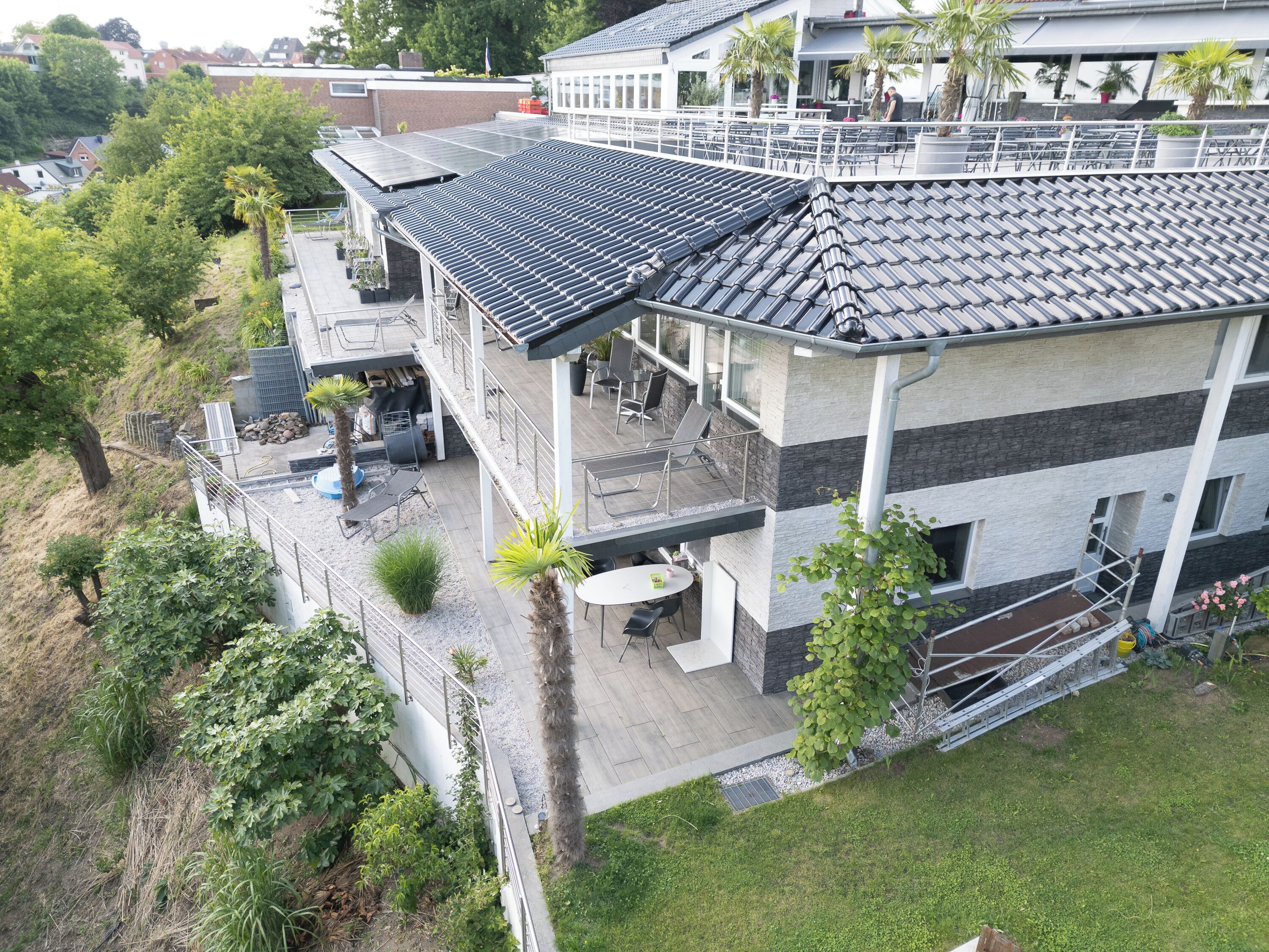 A multi-story building with a flat roof, outdoor seating area, and a small garden.