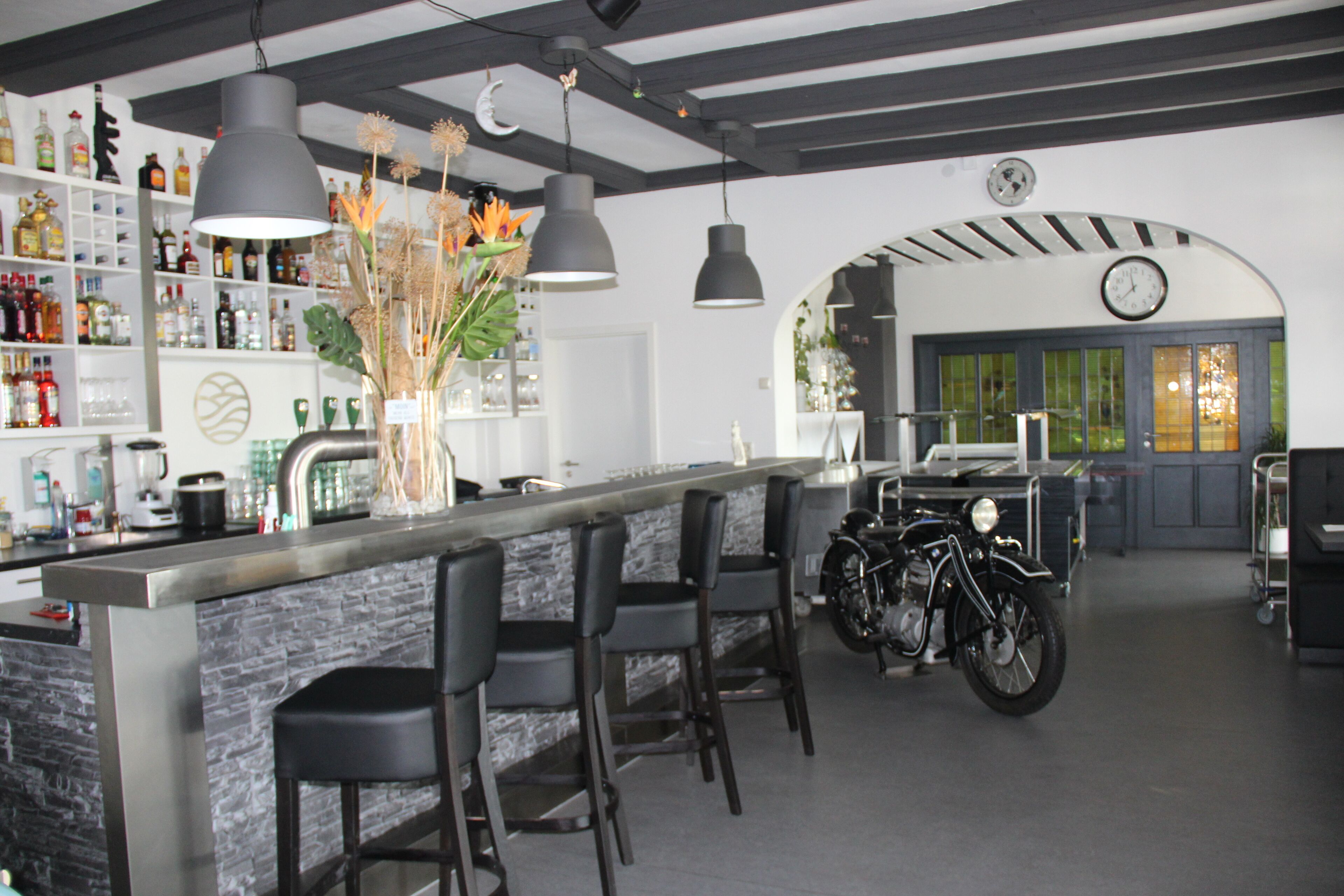 A bar area with a stone counter, black bar stools, and a motorcycle in the background.