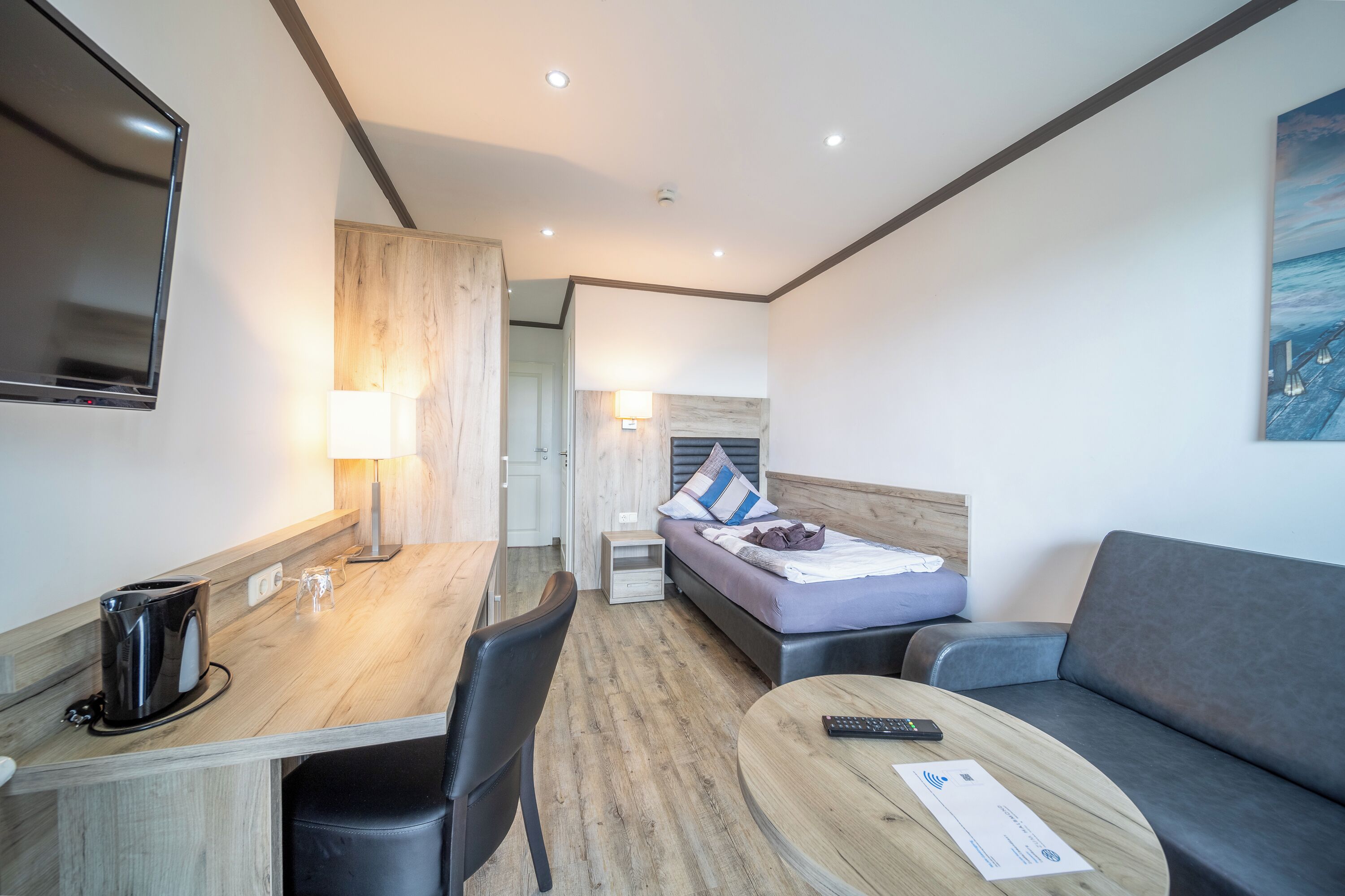 Una camera d'albergo moderna con una scrivania in legno, un divano, un letto con testiera e una TV a schermo piatto montata a parete.