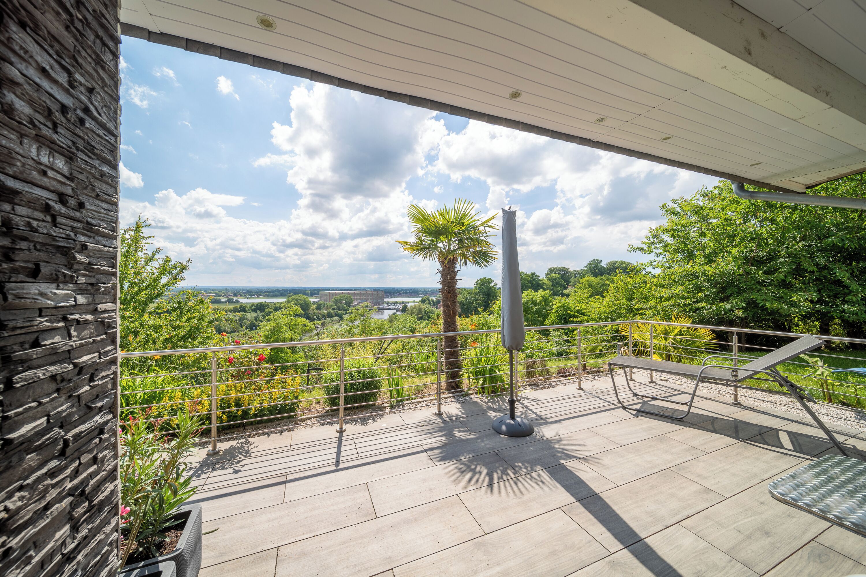 A terrace with a view of a landscape, a palm tree, and a metal railing.