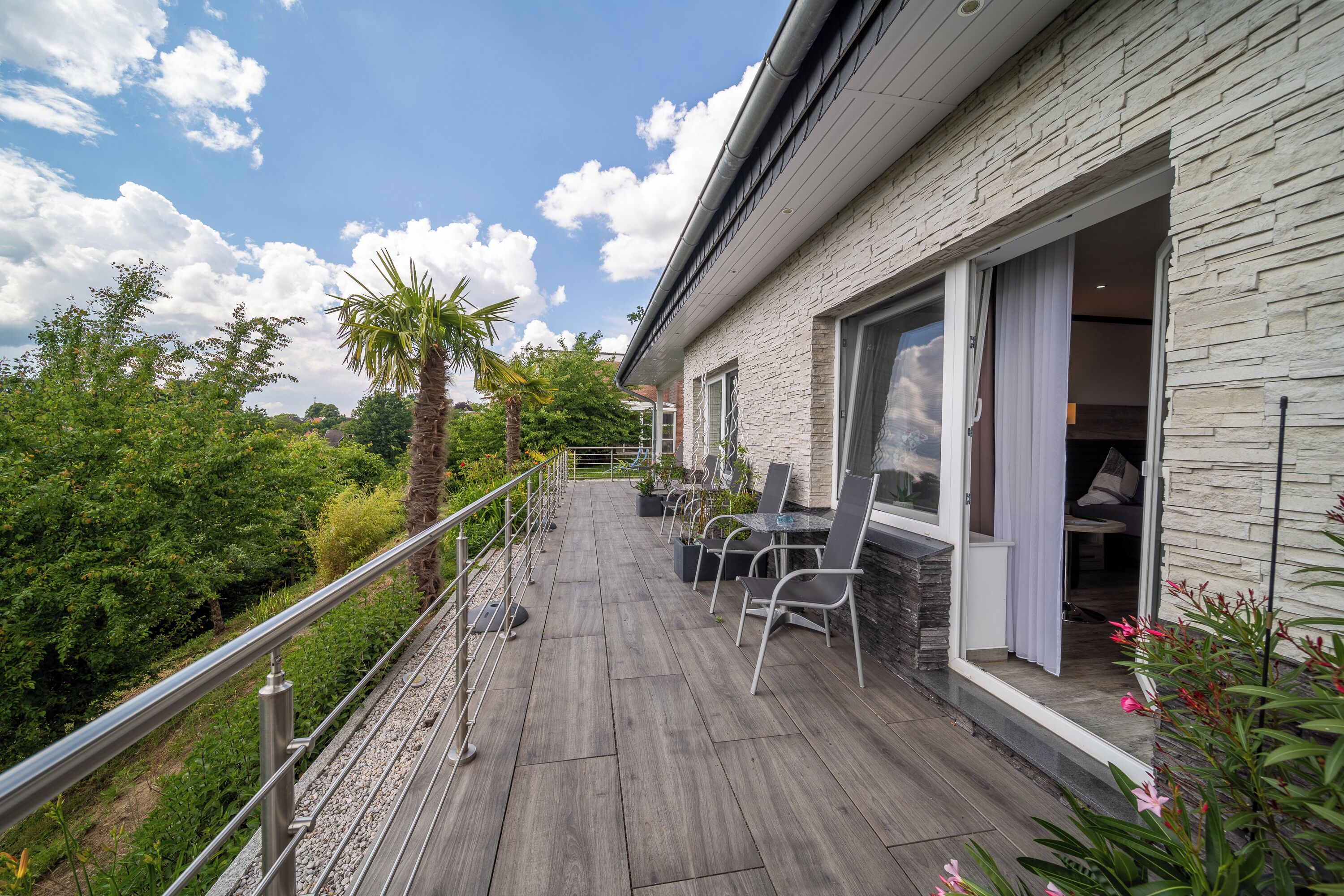 A modern outdoor patio with a stone wall, a wooden deck, and a seating area with chairs and a table.