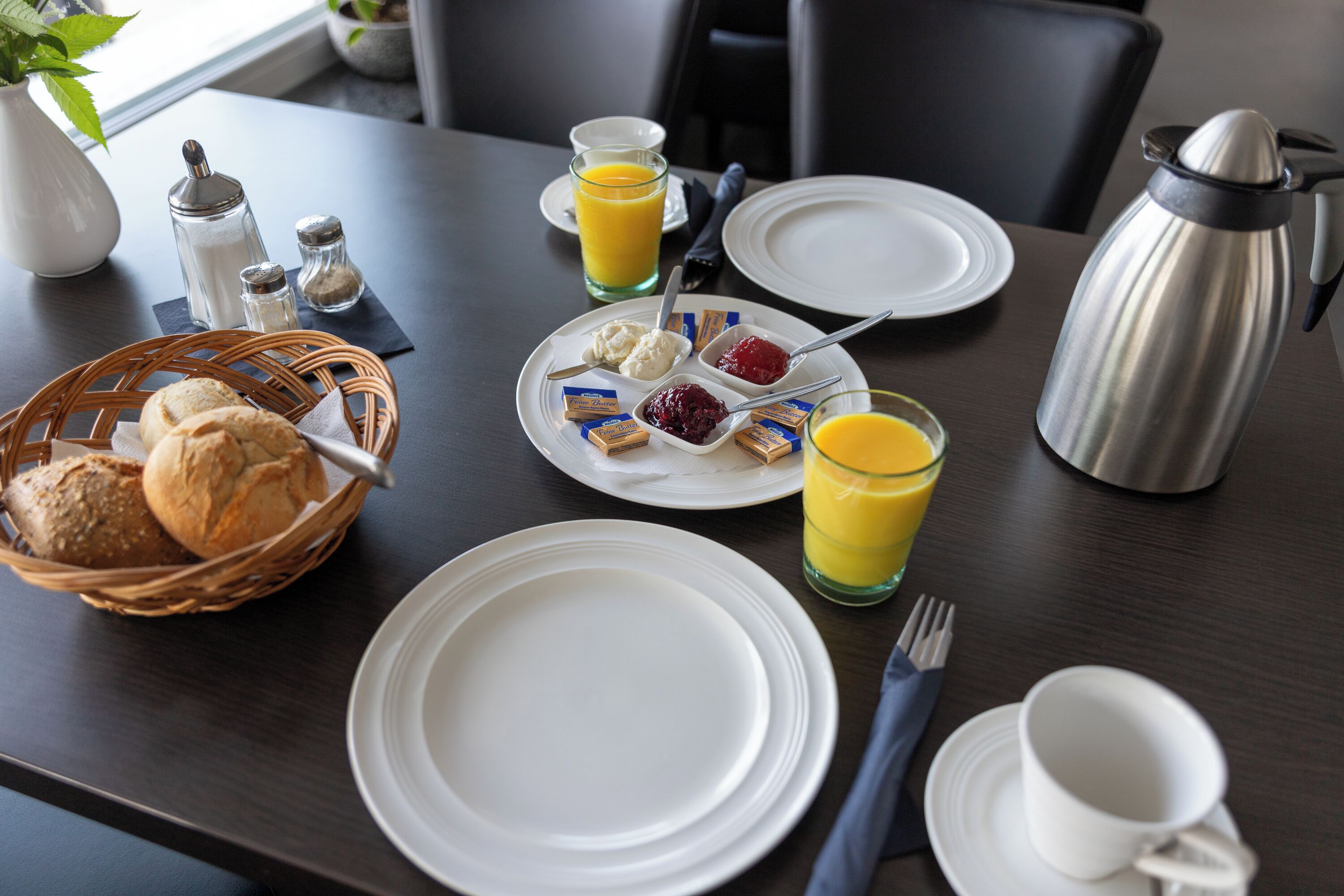 A breakfast table set with bread, butter, jams, and orange juice.