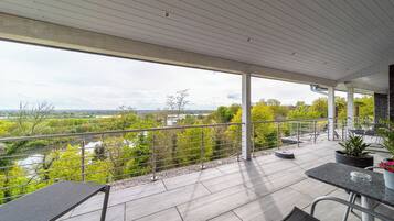 A covered outdoor area with a view of a river and greenery, featuring a table and chairs.